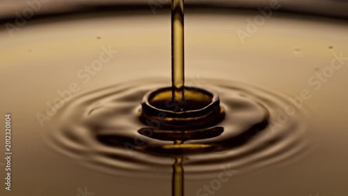 A single drop of golden liquid falls into a reflective surface