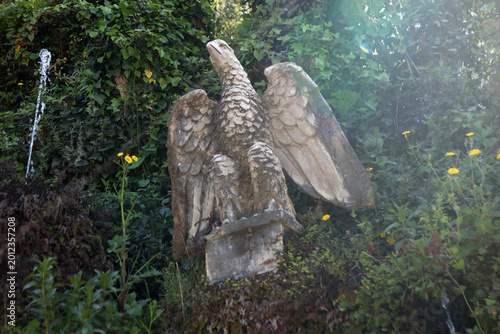 Photos Statua in pietra raffigurante un'aquila ad ali spiegate immersa nel verde della