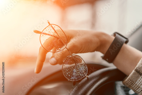 Eyeglasses raindrops car hand holding wet glasses over a steering wheel during a rainy golden hour commute