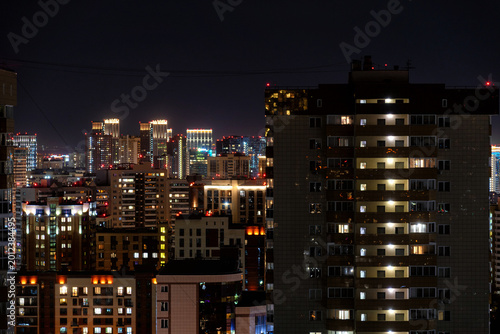 Modern residential apartment buildings illuminated at night. Urban cityscape featuring glowing windows, high-rise architecture, and city lights