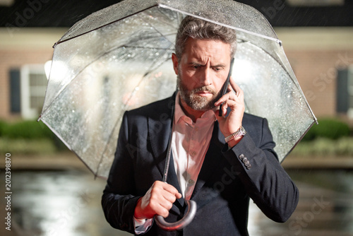 Foto Businessman talks on his phone under an umbrella on a rainy night