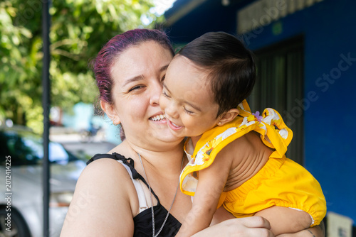 Fotografie Close-up of a mother with purple hair hugging her one-year-old daughter, both sharing an expression of happiness and joy outdoors