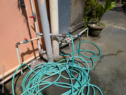 Foto Coiled garden hose rests beside outdoor pipes