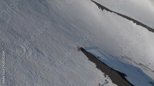 Aerial view of people standing on a volcanic patch amidst the snowy slopes of Mount Etna near Rifugio Sapienza in Nicolosi, Sicilia, Italy.