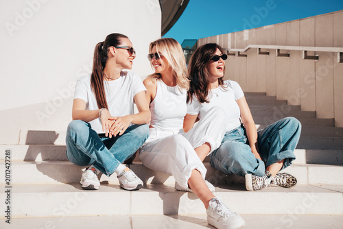 Three young beautiful smiling hipster female in trendy summer white t-shirt  and jeans clothes. Sexy carefree women posing in street. Positive models having fun, going crazy. In sunny day