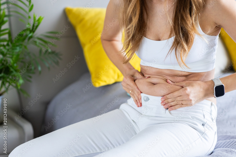 Fototapeta premium Young woman examining her midsection at home