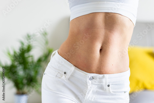 Close-up of woman's toned abdomen in white clothing indoors