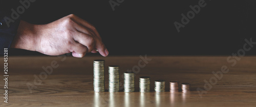 Hand pointing at stacks of coins on wooden table with dark background, symbolizing financial planning, savings, investment growth, business strategy, and money management concepts