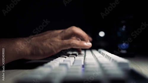 Hands typing on keyboard in dark room, Close-up of hands typing on a white computer keyboard in dark room