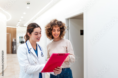 Female doctor in white coat discussing medical results on a clipboard with a patient in a hallway. Healthcare and medicine concept, professional consultation, explaining diagnosis in a clinic.