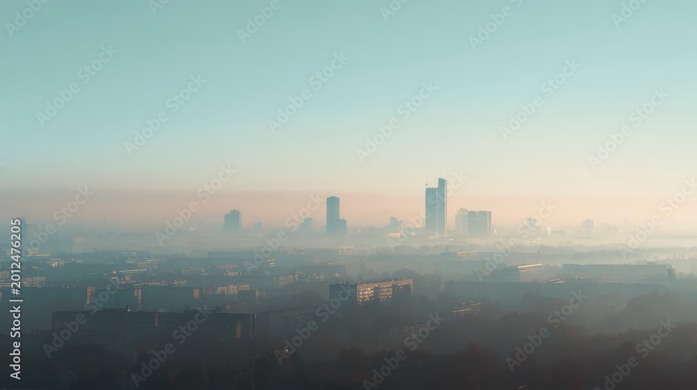 Fototapeta premium Urban buildings and residential structures rise above a thick blanket of morning fog, with sunlight casting a warm glow across the hazy atmosphere and urban landscape