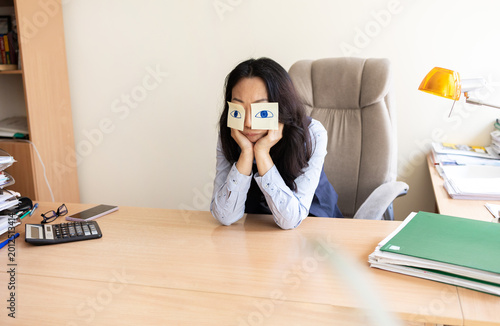 Obraz na plátně Asian woman with fake eyes drawn on sticky notes snoozing at workplace in office