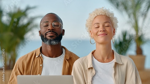 diverse man and woman are shown sitting together with their eyes closed and peaceful expressions. They appear to be practicing mindfulness or taking a mental break in an outdoor setting featuring 