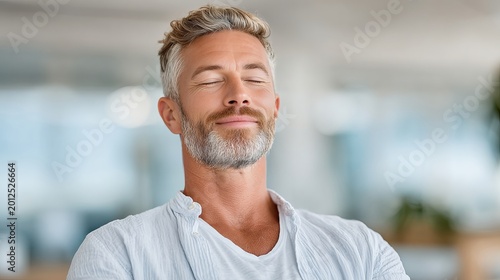 A composed, middle-aged man with gray hair breathes deeply with eyes closed, embodying calmness, mindfulness, and professional serenity in a softly blurred office environment.
