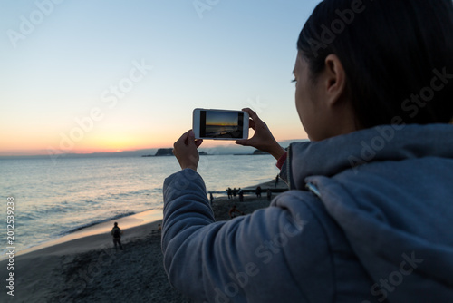 Bild auf Leinwand Back view of person taking picture of calm sea during golden hour