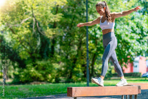 Bild auf Leinwand Athletic woman stepping forward on narrow beam, focusing on balance, coordination and functional outdoor fitness training
