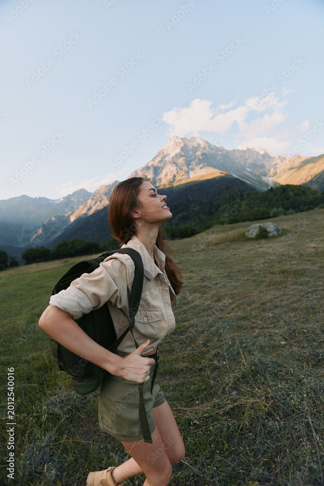Naklejka premium Active woman hiking outdoors with backpack in alpine meadow, mountains in the background. Adventure, nature, wellness, and outdoor lifestyle for motivation and balance.