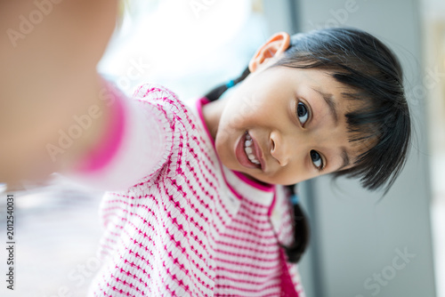 Asian little girl holding camera taking selfie indoor with smile