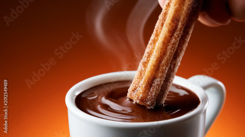 Steaming hot chocolate with churros on warm orange background