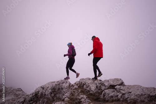Fotografie Couple Hiking on Foggy Mountain Ridge in Winter Jackets During Outdoor Adventure