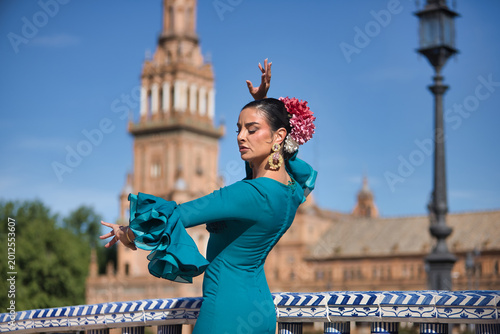 Young, brunette, Andalusian woman, beautiful, wearing a green flamenco dress and flowers in her hair, dancing flamenco on a pretty bridge in Spain Square in Seville.