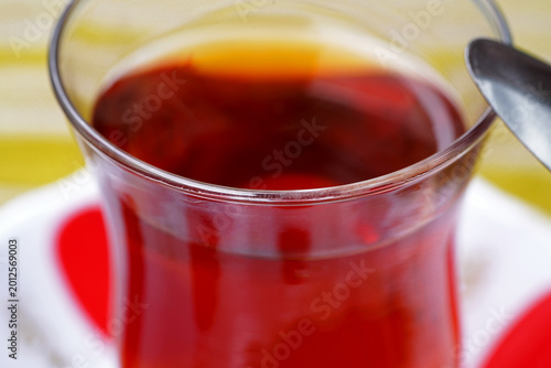 Close-up of traditional Turkish tea in glass cup. Hot red tea with spoon and soft background. Warm beverage composition with cozy atmosphere and cultural style