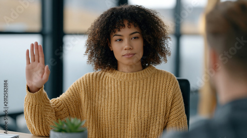Female therapist seated across from a client, gently holding up one palm in a calm stop gesture while maintaining steady eye contact, minimal office setting, afternoon light through frosted glass, a