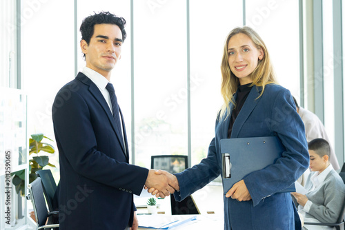 Businesswoman and businessman leader looking at camera in modern office with businesspeople working at the background. Teamwork concept. 