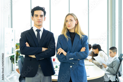 Businesswoman and businessman leader looking at camera in modern office with businesspeople working at the background. Teamwork concept. 