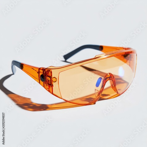Bright orange protective eyewear casts a sharp shadow on a white surface