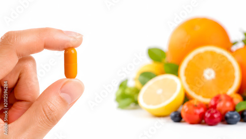 Close-up of hand holding Vitamin C capsule with medical icons, healthy immune system and skincare benefit concept with fresh citrus background and copy space.