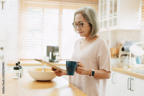 Senior Asian woman using Tablet computer modern technology to learning cook food menu in kitchen