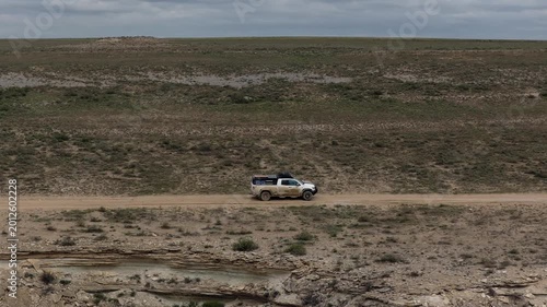 Aerial view of an off-road vehicle driving on a dirt road through the rocky desert landscape of Bozjyra with a cloudy sky in Aktau, Mangystau Region, Kazakhstan.