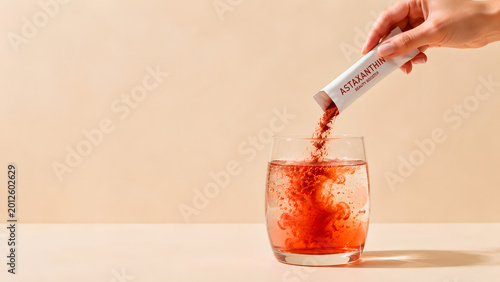 Astaxanthin powder pouring into water mockup, premium commercial action of red antioxidant supplement with massive copy space on beige background.