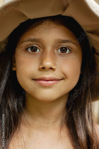 Portrait of a happy smiling girl wearing a sun hat outdoors. Close-up of a cheerful child with natural light and warm tones. Concept of childhood, happiness, innocence and carefree lifestyle.