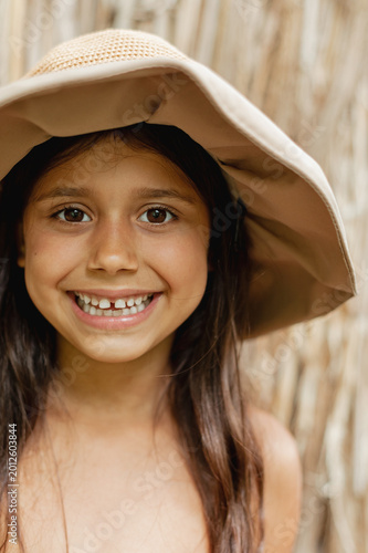 Portrait of a happy smiling girl wearing a sun hat outdoors. Close-up of a cheerful child with natural light and warm tones. Concept of childhood, happiness, innocence and carefree lifestyle.