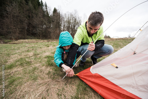 Exciting camping adventure unfolds as a father and daughter set up a tent amidst the serene beauty of nature on a cloudy day in the great outdoors