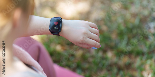 Asian woman checking heart rate on smartwatch during outdoor fitness activity