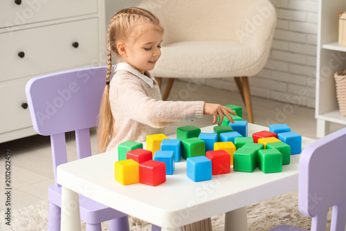 Cute little girl playing with plastic cubes at table in children's room