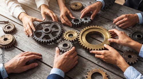 Diverse business people's hands carefully arranging various metal gear components on a light wooden table.