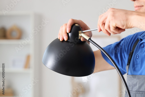 Foto Male electrician tightening screw in desk lamp with screwdriver, closeup