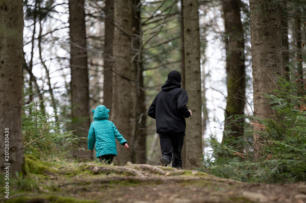 Fototapeta premium Meandering through a tranquil forest path alongside a child and their guardian, we relish the refreshing coolness of an early spring afternoon