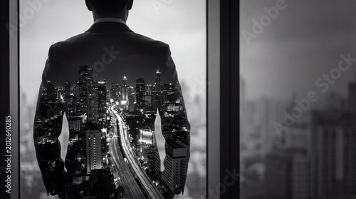 Foto Black and white double exposure of a businessman gazing out a window, merged with a dynamic city night skyline