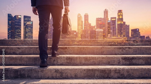 Photography Businessman with briefcase walking up concrete stairs towards a vibrant city skyline at sunset