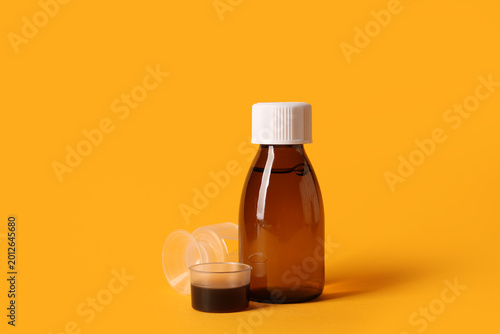 Fotografie Bottle of cough syrup and measuring cups on orange background