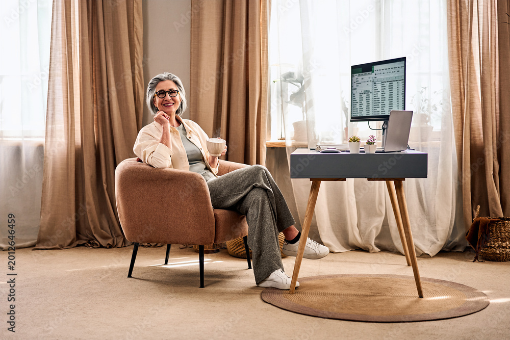 Obraz premium Senior woman working from home with coffee in cozy home office.