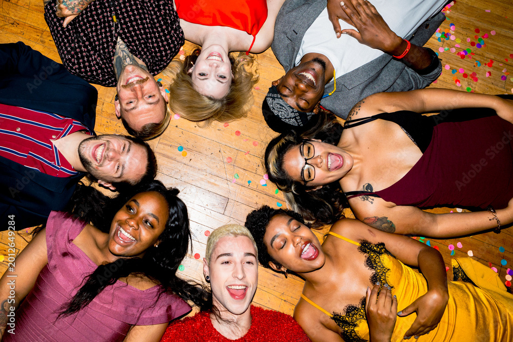 Fototapeta premium A diverse group of people lying in a circle on a wooden floor, smiling and laughing, surrounded by colorful confetti.