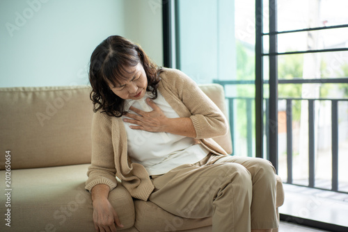Принти на полотні Unhappy Asian senior woman coughing with illness and fatigue while sitting alone