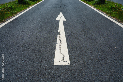 An asphalt road stretches into the distance with a painted white arrow, symbolizing motivation, progress and the concept of continuous growth and forward movement.