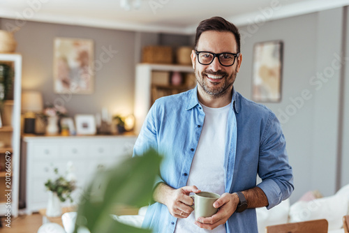 Foto Smiling Casual Man Drinking Coffee at Home in Bright Cozy Living Room
